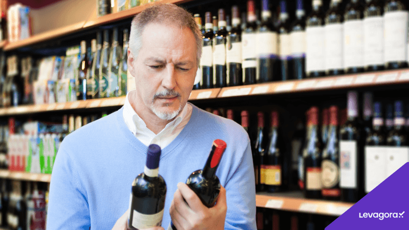 Dificuldade na escolha de vinhos impulsiona popularidade dos kits de vinho Homem analisando diferentes rótulos de vinho em loja, representando a dificuldade de escolher o vinho ideal