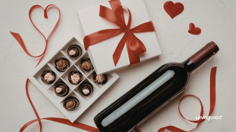 Vinho e Chocolates: O Presente Perfeito Visão superior de uma garrafa de vinho tinto ao lado de uma caixa de trufas de chocolate e uma fita vermelha em formato de coração, representando a elegância de um kit de vinho para presente romântico.